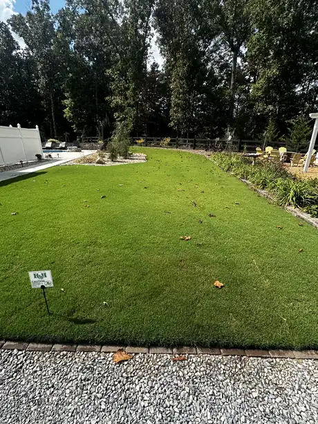A backyard lawn beside a pool with an H&H "just treated" sign in place