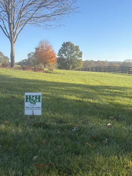 An H&H yard sign on a lawn with fall color along the fence line