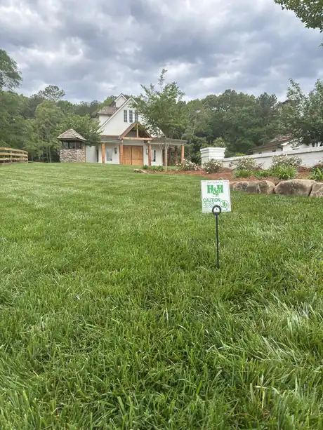A dense, freshly treated tall fescue lawn with an H&H sign and the estate behind