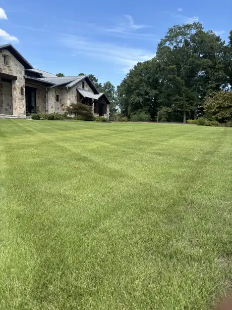 A wide open Zoysia lawn in front of a stone house