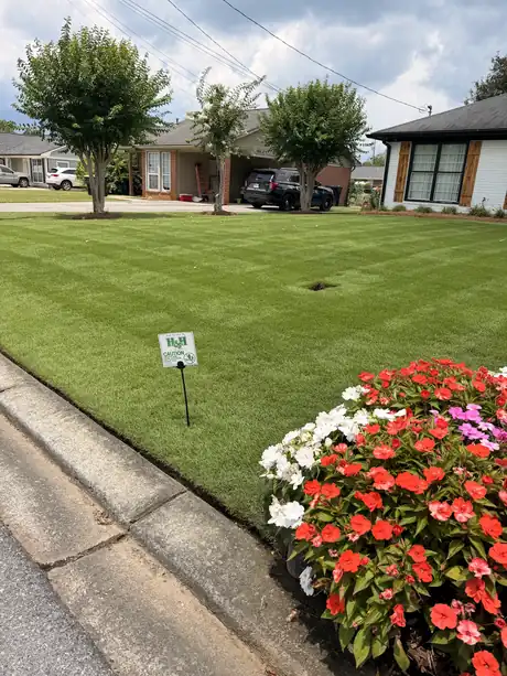 A striped, weed-free front lawn with an H & H Lawn Care sign at the curb